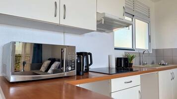 A modern kitchen with white cabinets, a wooden countertop, a built-in microwave, a coffee maker, and a window with blinds.