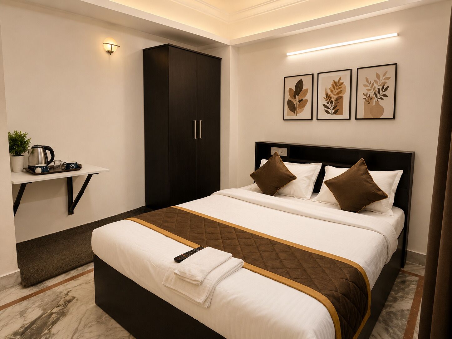 A modern hotel room with a large bed, a desk with a kettle, and framed artwork on the wall.