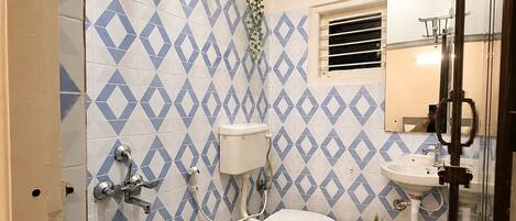 A bathroom with a toilet, bidet, and shower with a white and blue diamond-patterned tile wall.