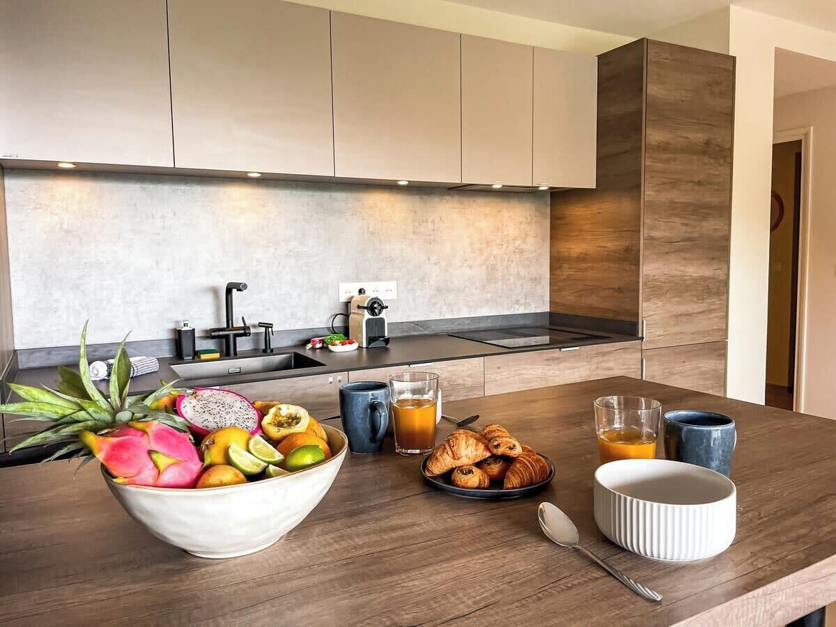 Een moderne keuken met een houten aanrecht, een schaal fruit, croissants en een kop koffie.