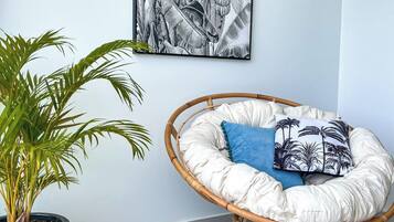 A room with a rattan chair, a potted plant, and a wall-mounted artwork.