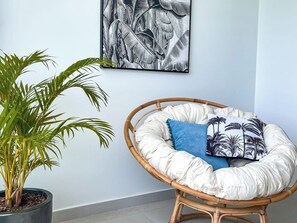 Um quarto com uma cadeira de vime, uma planta em vaso e uma obra de arte na parede.
