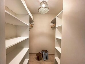 Um closet espaçoso com diversas prateleiras e espaço para pendurar roupas, piso de madeira e uma luminária.