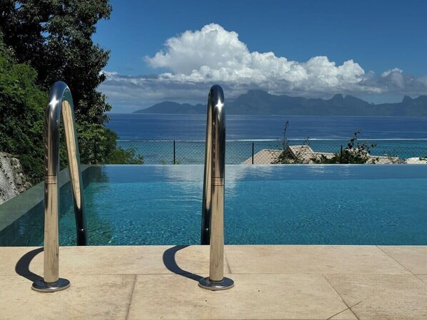 A swimming pool with a clear view of the ocean and mountains in the background.