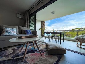 A modern living room with a sofa, a round table, and a balcony with a view.