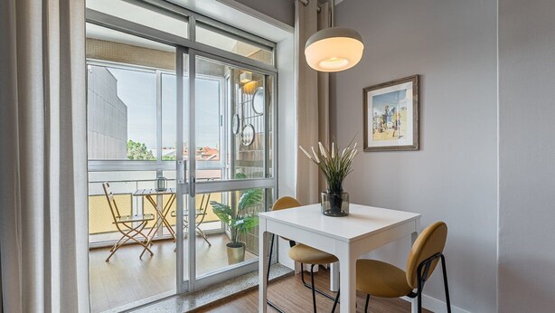 Ein modernes Zimmer mit einem weißen Tisch, zwei Stühlen, einer Topfpflanze, einer Hängelampe und einem gerahmten Bild an der Wand.