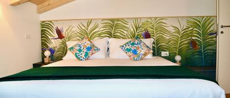 A bed with a green bedspread, two decorative pillows, and a headboard with a tropical leaf pattern.