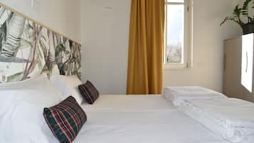 Ein Hotelzimmer mit einem großen Bett, zwei Kissen, einem Fenster mit Vorhängen und einer Pflanze auf einem Schrank.