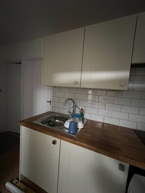 Una pequeña cocina con armarios blancos, un lavamanos de acero inoxidable y una encimera de madera.