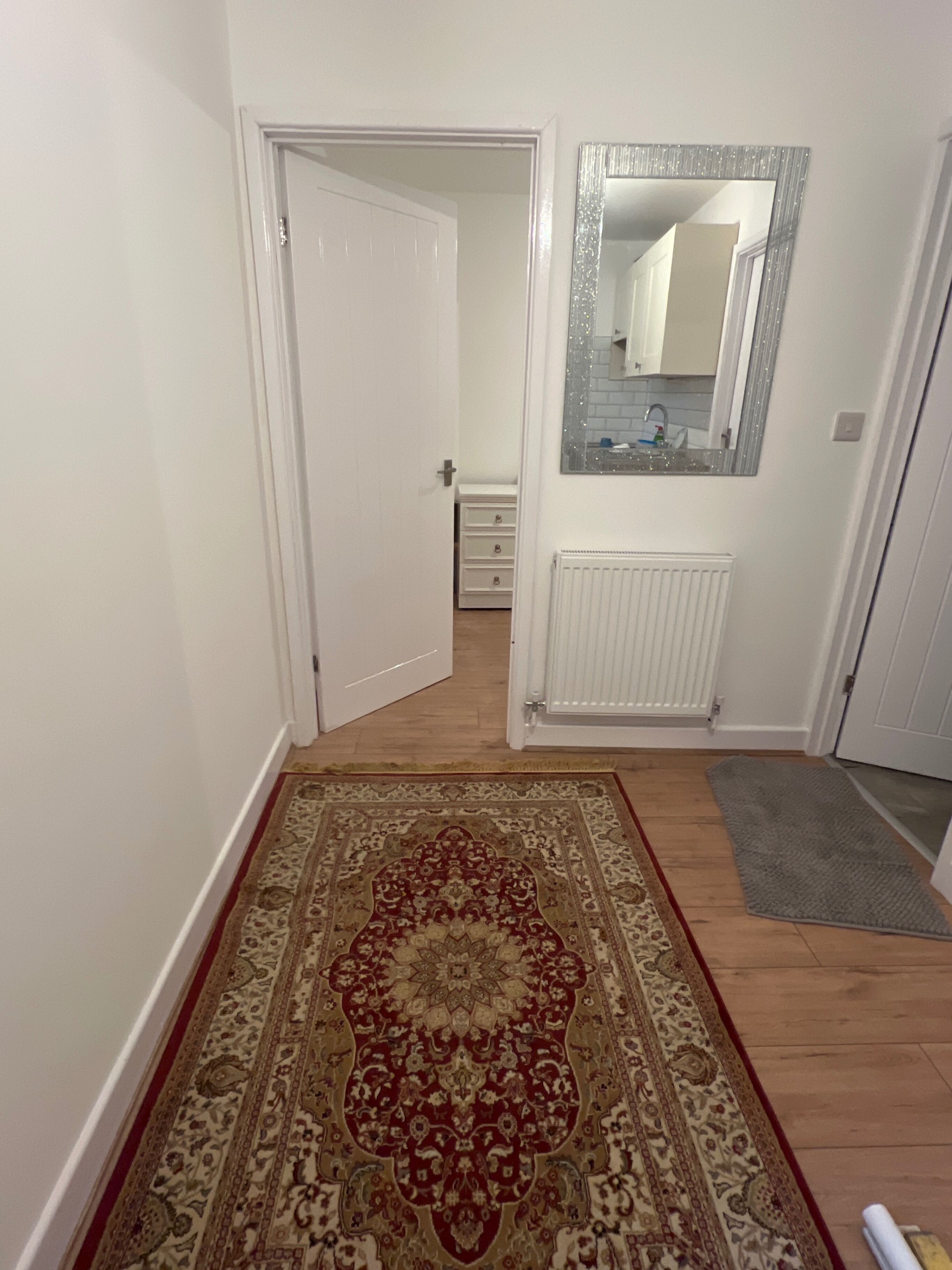 A hallway with a patterned rug, a white radiator, and a mirror on the wall.