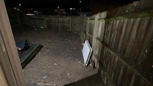 Un espacio al aire libre con poca luz, valla de madera, portón metálico y suelo de concreto.