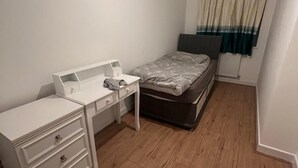 Un dormitorio pequeño y ordenado con una cama individual, un aparador blanco con cajones y una ventana con cortinas.