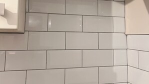 Una esquina de una habitación con paredes de azulejos blancos y un enchufe a la vista.