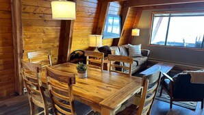 L’intérieur d’un chalet accueillant, avec une table à manger en bois, des chaises, un canapé et une grande fenêtre.