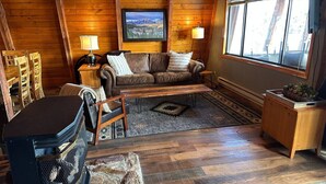 L’intérieur d’un chalet accueillant, avec un plafond en bois, un canapé, une table basse, une cheminée et une fenêtre donnant sur le paysage extérieur.