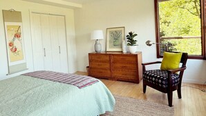 A bedroom with a bed, a dresser, a chair, a lamp, and a window with a view of trees. - Raven's View - Walk to town, beach, restaurants (Inverness)