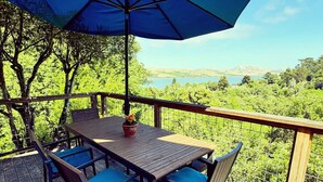 A wooden deck with a table and chairs, overlooking a scenic view of trees and a body of water. - Raven's View - Walk to town, beach, restaurants (Inverness)