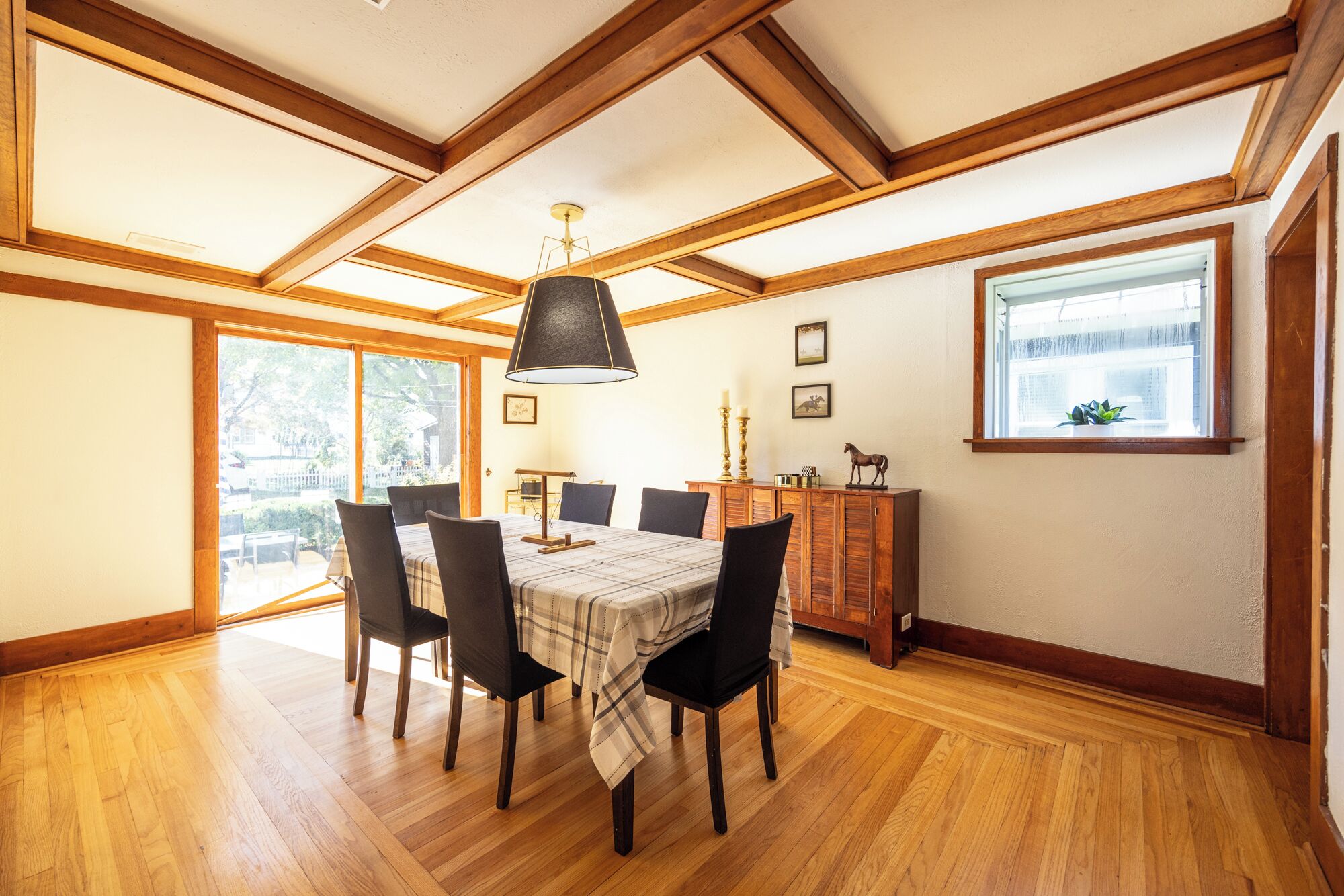 Een eethoek met een houten tafel, stoelen en een kroonluchter. Er is een raam met uitzicht op buiten.