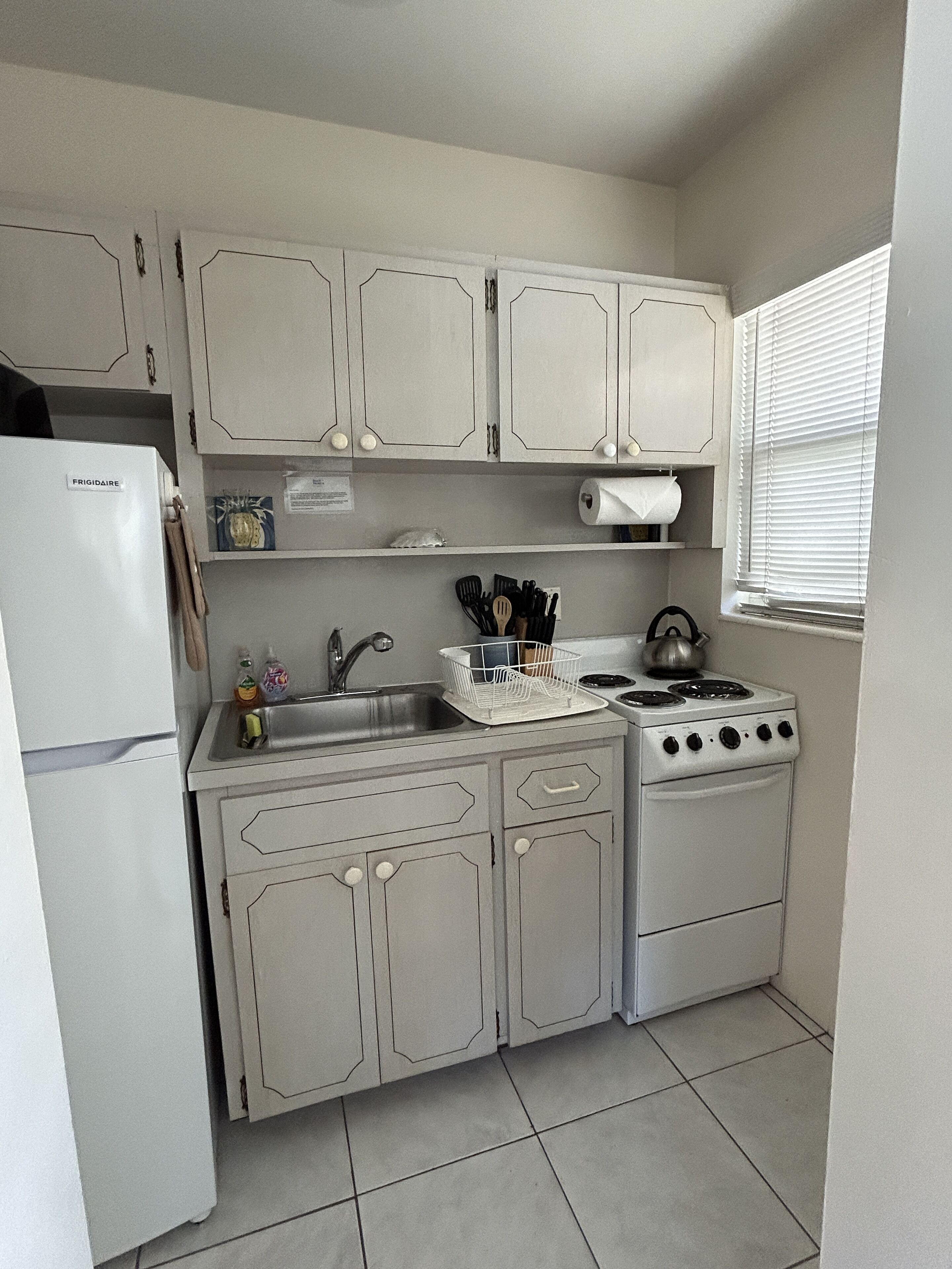 A compact kitchen with white cabinets, a refrigerator, a stove, and a sink.