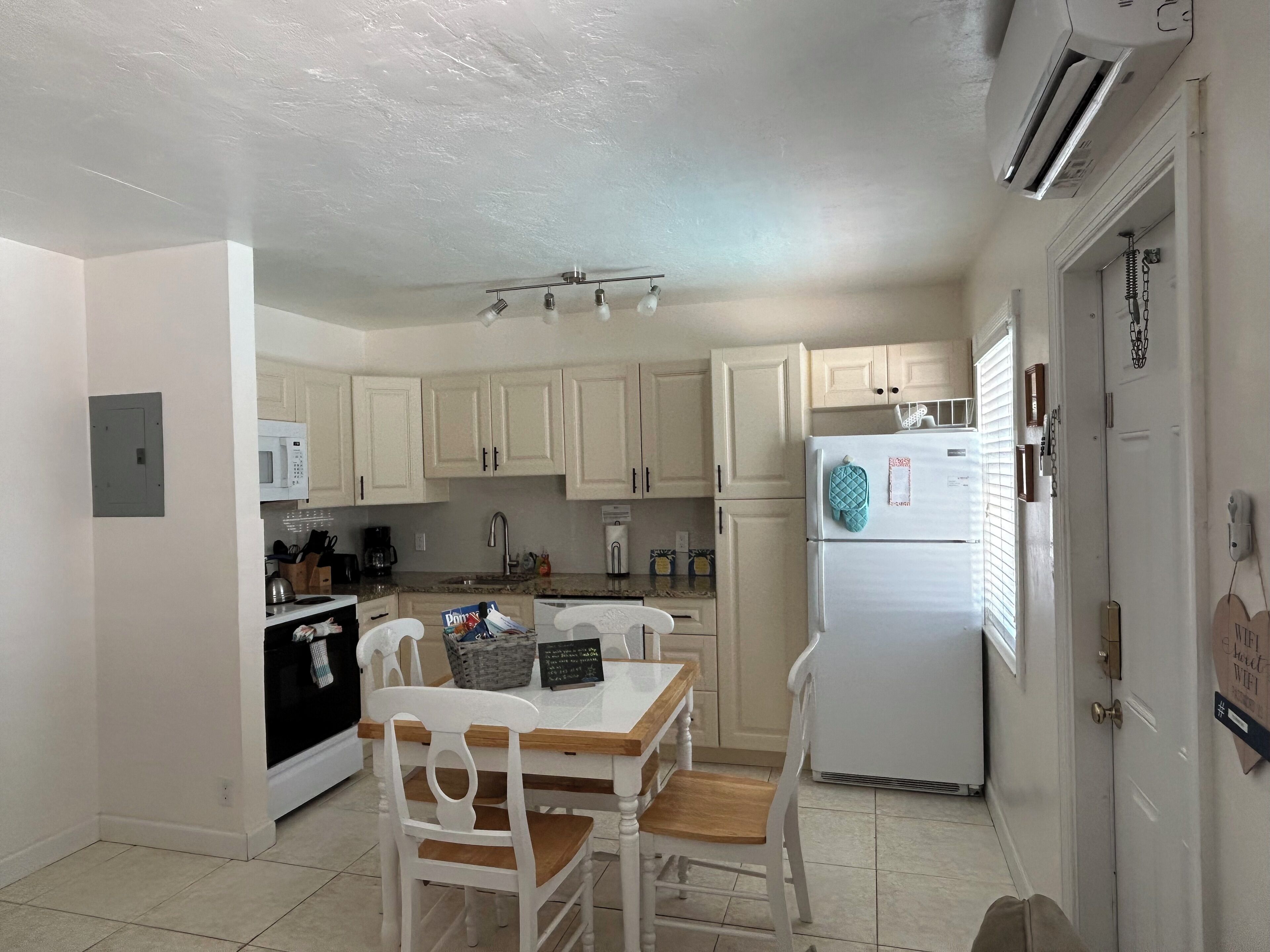 A compact kitchen with white cabinets, a white refrigerator, and a dining table with two chairs.