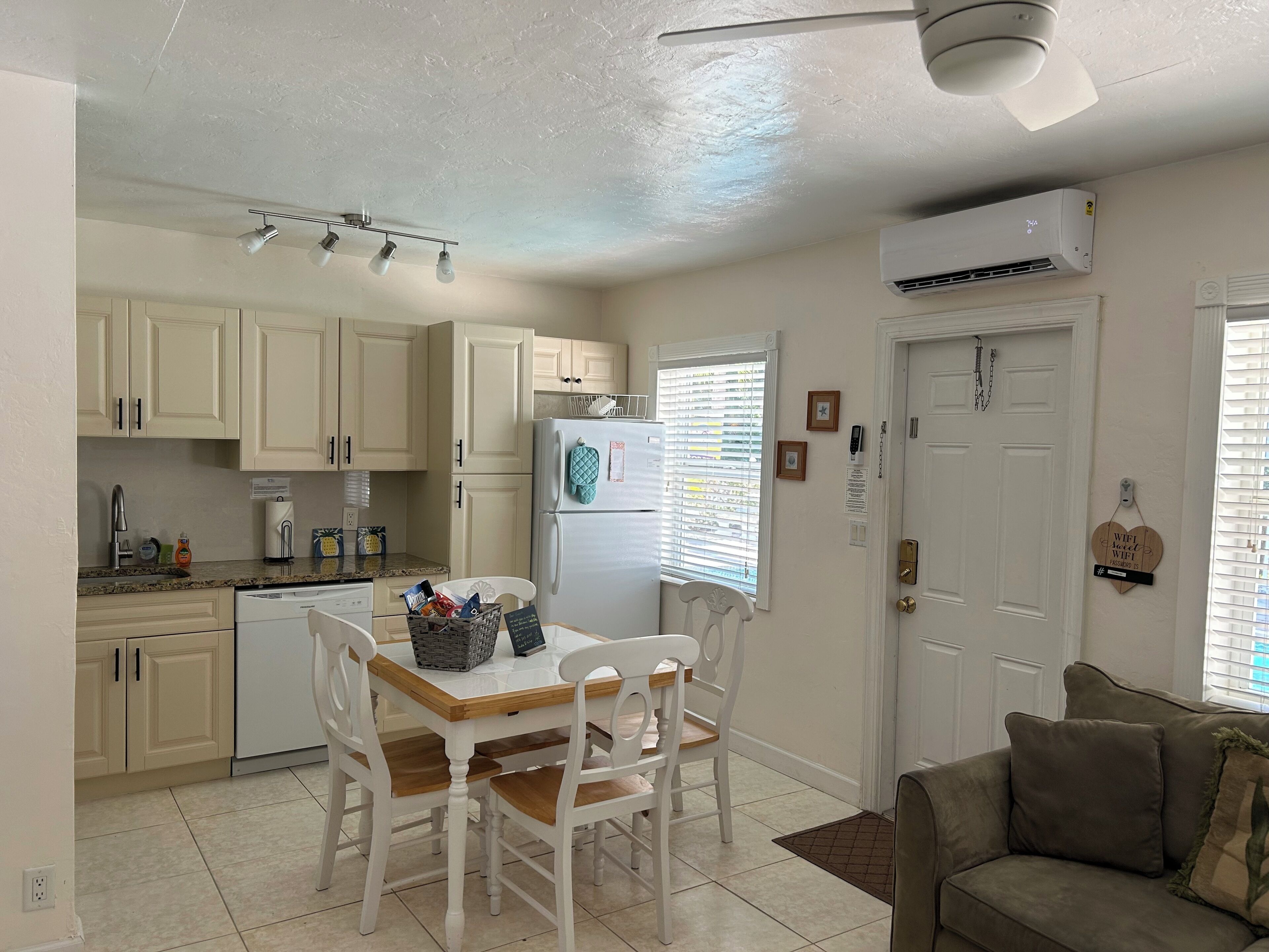 Une cuisine avec des meubles blancs, un réfrigérateur, une table à manger avec des chaises et un ventilateur de plafond.