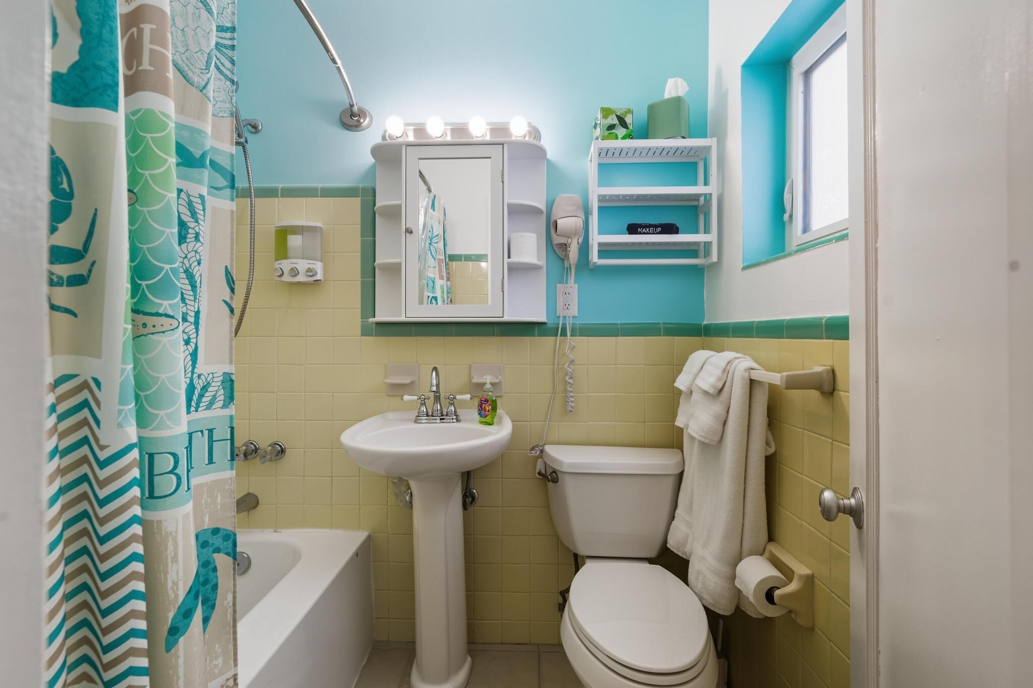 Un baño con bañera, lavabo, inodoro, tocador con espejo y cortina de ducha.