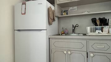 Une cuisine de taille réduite, avec un réfrigérateur blanc, des placards dotés de poignées, un évier et divers ustensiles de cuisine.