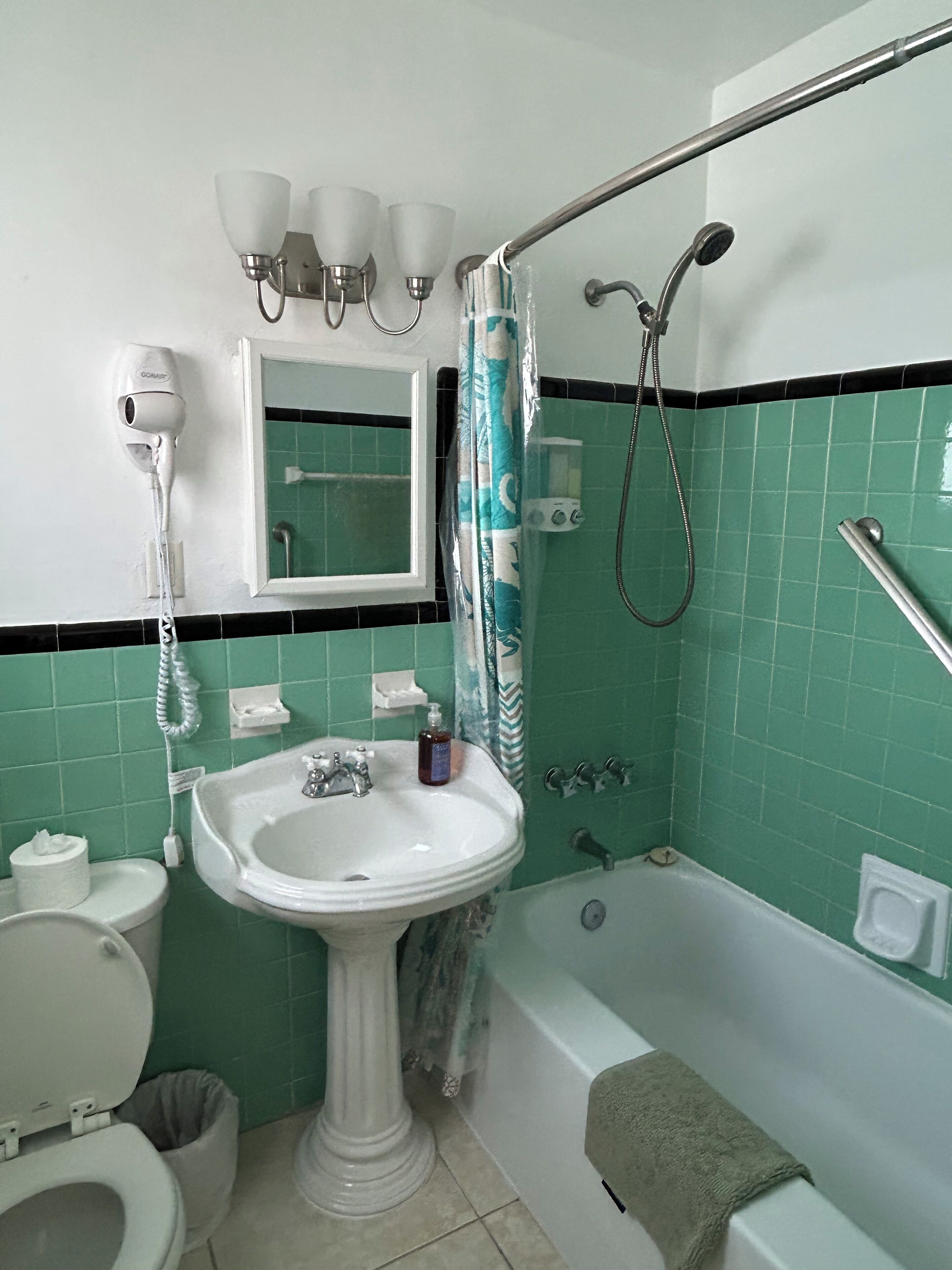 A bathroom with a pedestal sink, a toilet, a bathtub, and a shower with a handrail.