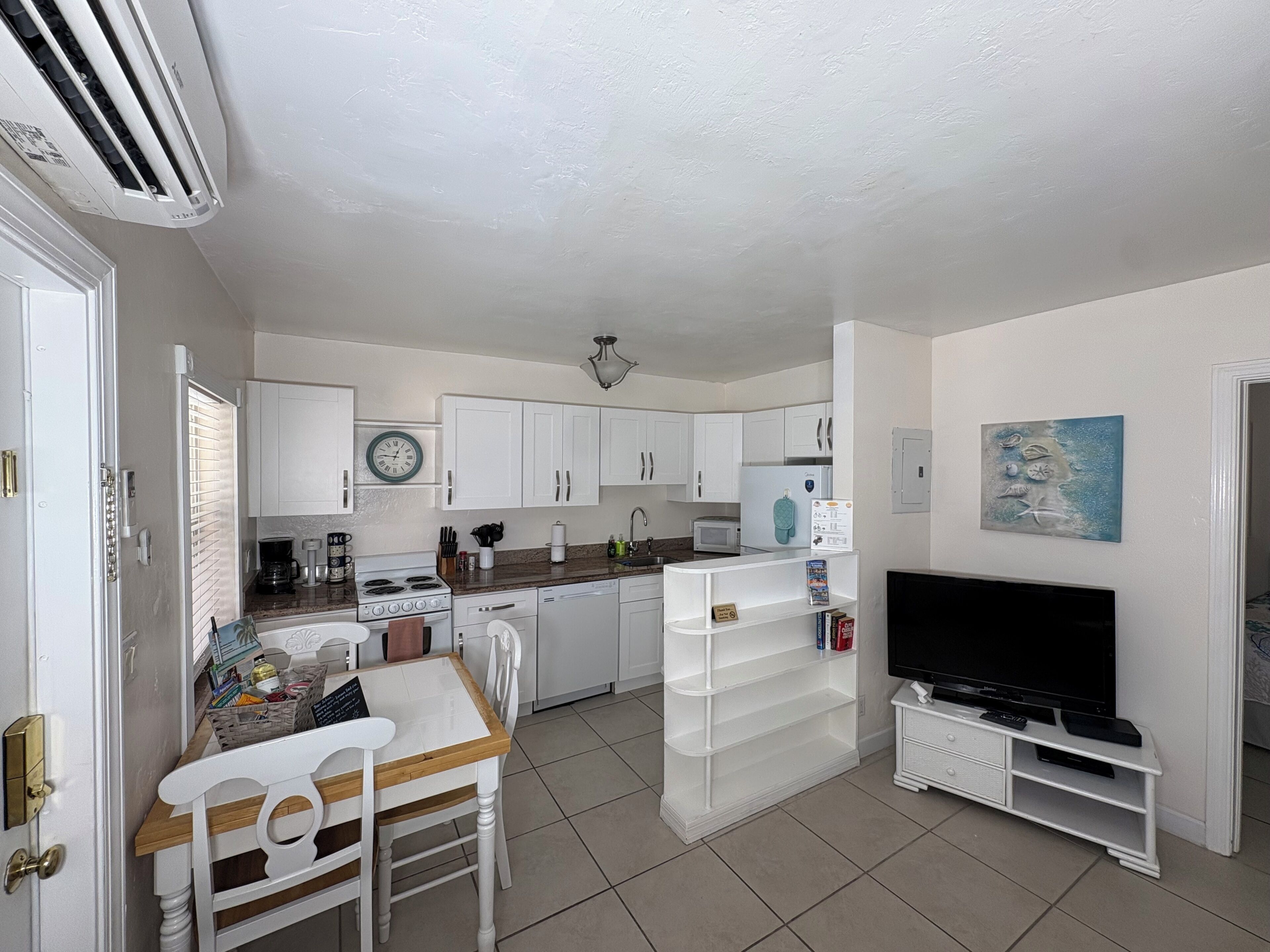 A compact kitchen with white cabinets, a stove, a sink, and a dining area with a table and chairs.