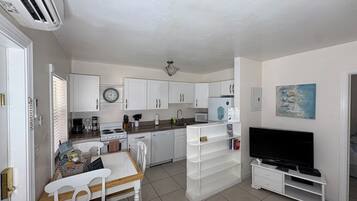 A compact kitchen with white cabinets, a stove, a sink, and a dining area with a table and chairs.