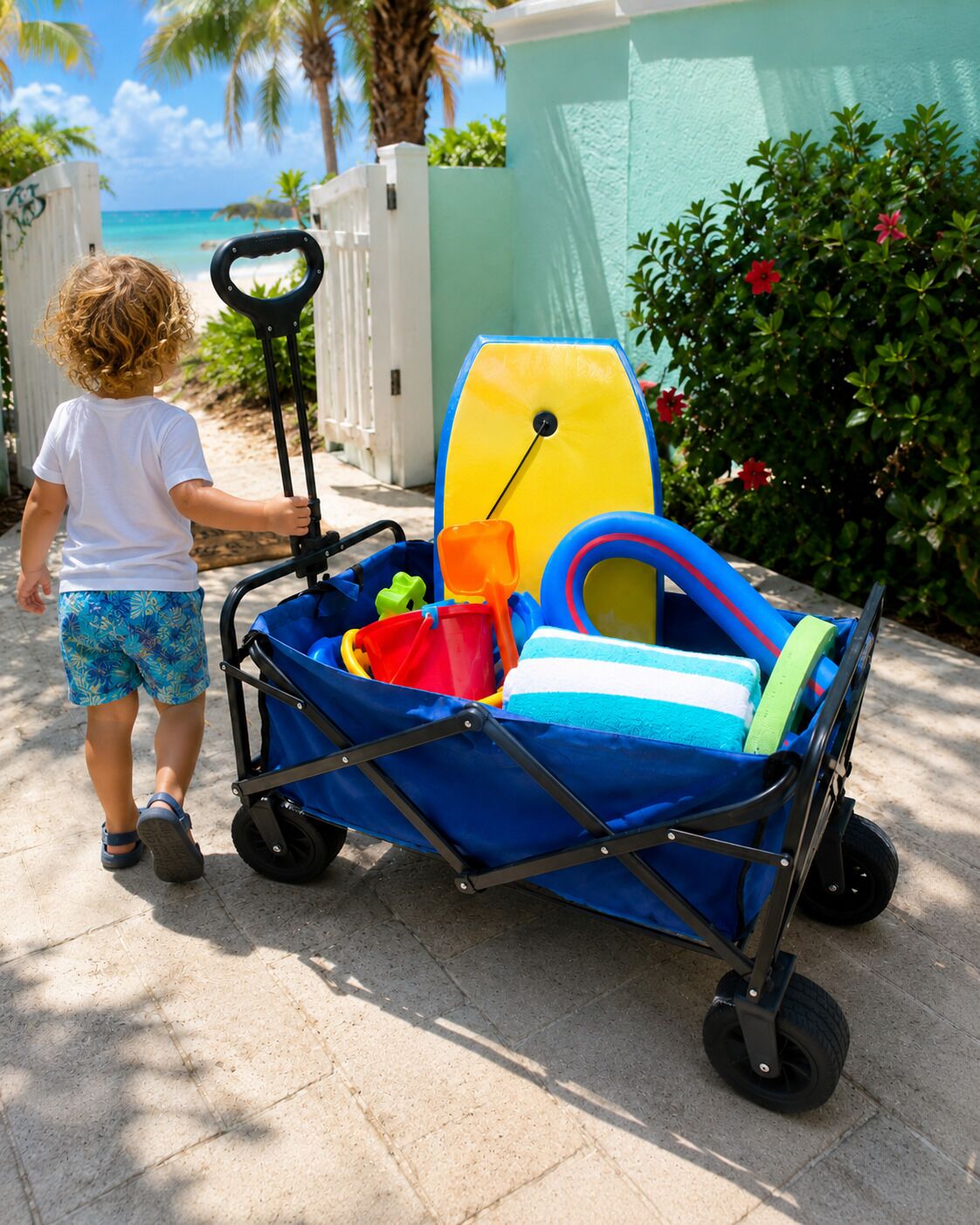 Un enfant poussant un chariot de plage contenant une planche de surf et des jouets de plage.