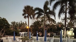 A swimming pool with lounge chairs and umbrellas, surrounded by palm trees and a white fence. - Bahama Beach Club Pompano (Pompano Beach)