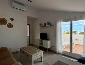 A living room with a sofa, a coffee table, a TV on a stand, and a sliding glass door leading to an outdoor area.