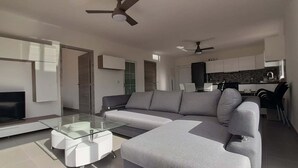 Ein modernes Wohnzimmer mit einem Flachbildfernseher, einem Glastisch und einem grauen Ecksofa.