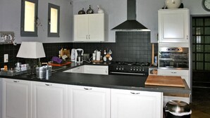 A kitchen with white cabinets, a black countertop, a stove, a sink, and a window with natural light. - La Caracole :Provencal villa with heated pool, tennis court, nature at your doorstep (Caseneuve)
