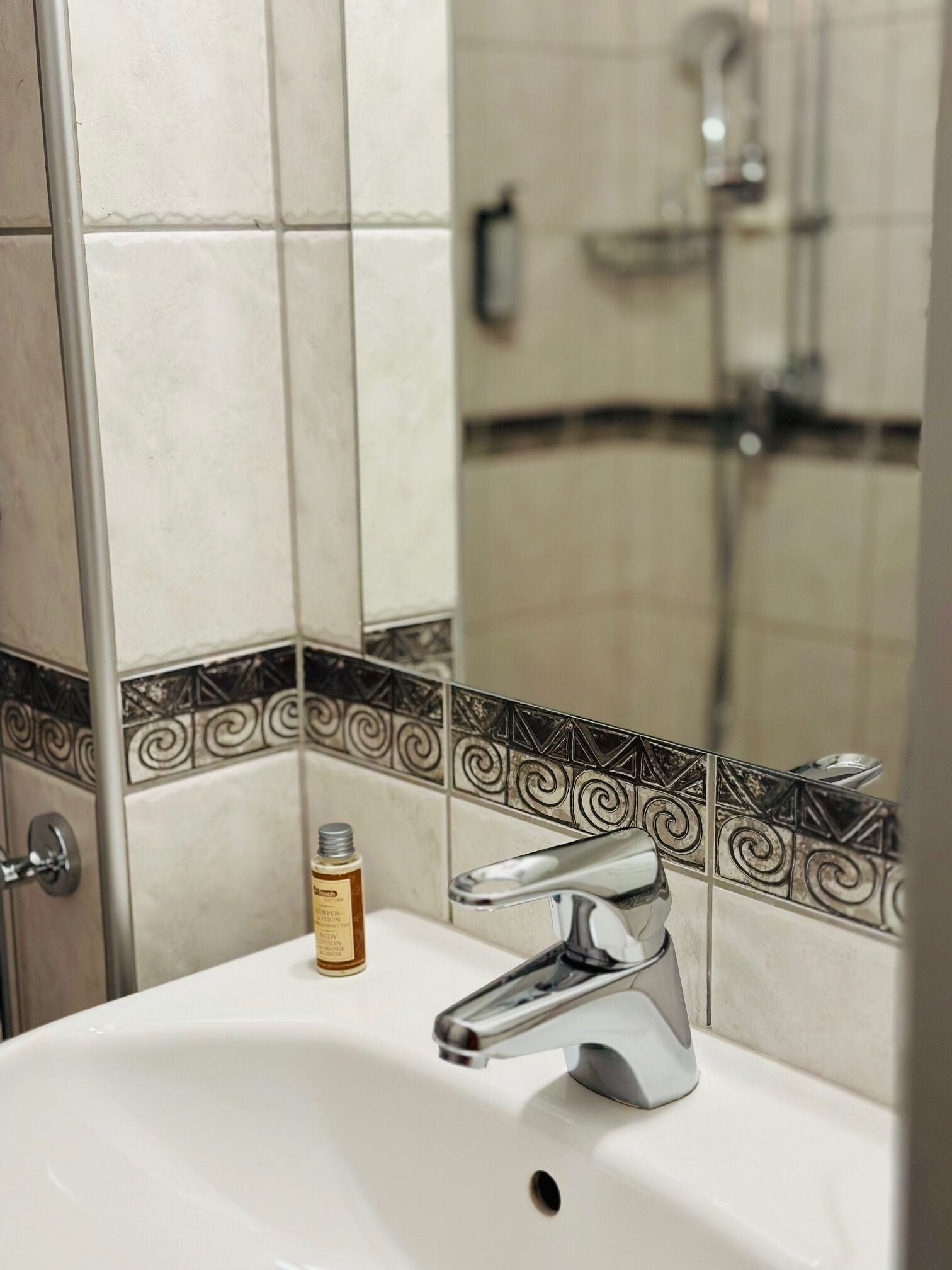 A bathroom with a white sink, chrome faucet, and decorative black and white tiles.