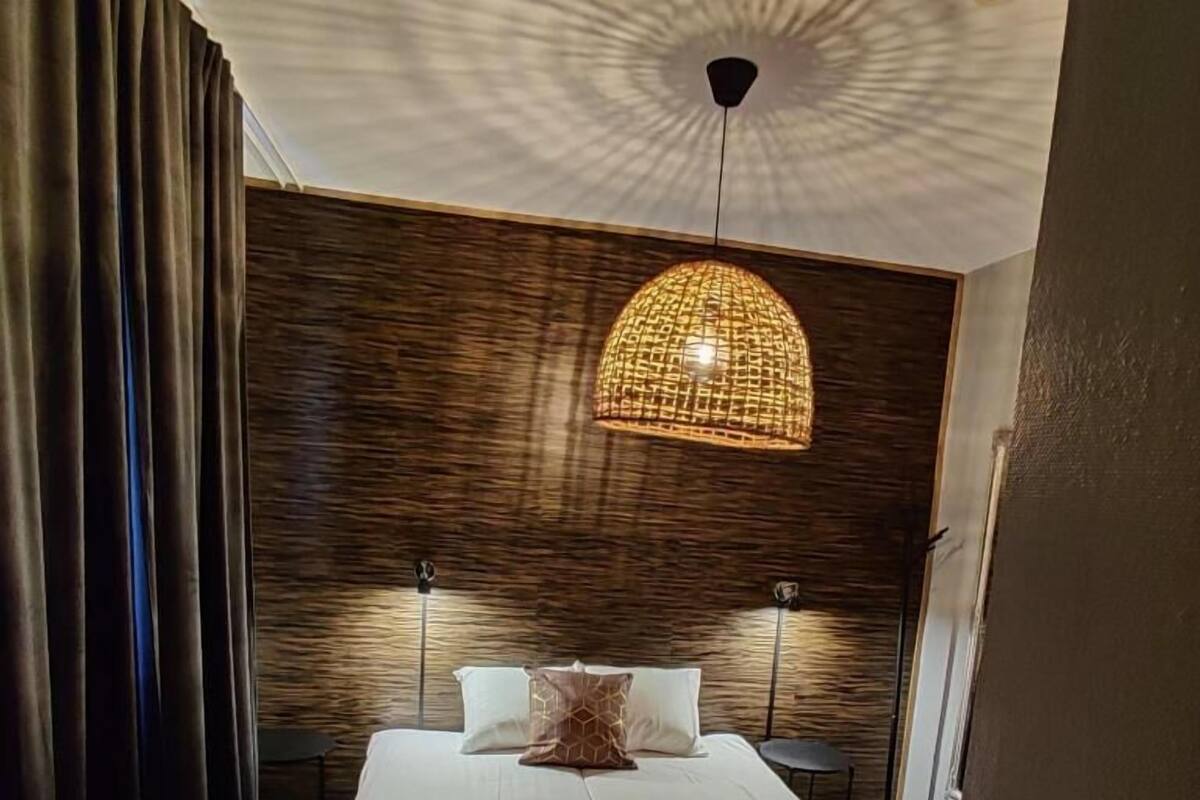 Un lit bien fait, avec une tête de lit texturée, deux lampes de chevet et une suspension en fibres tressées au-dessus.
