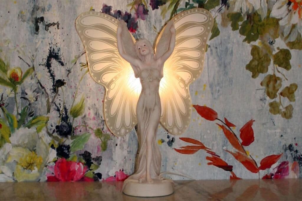 A decorative angel statue with wings, placed on a table against a floral background.