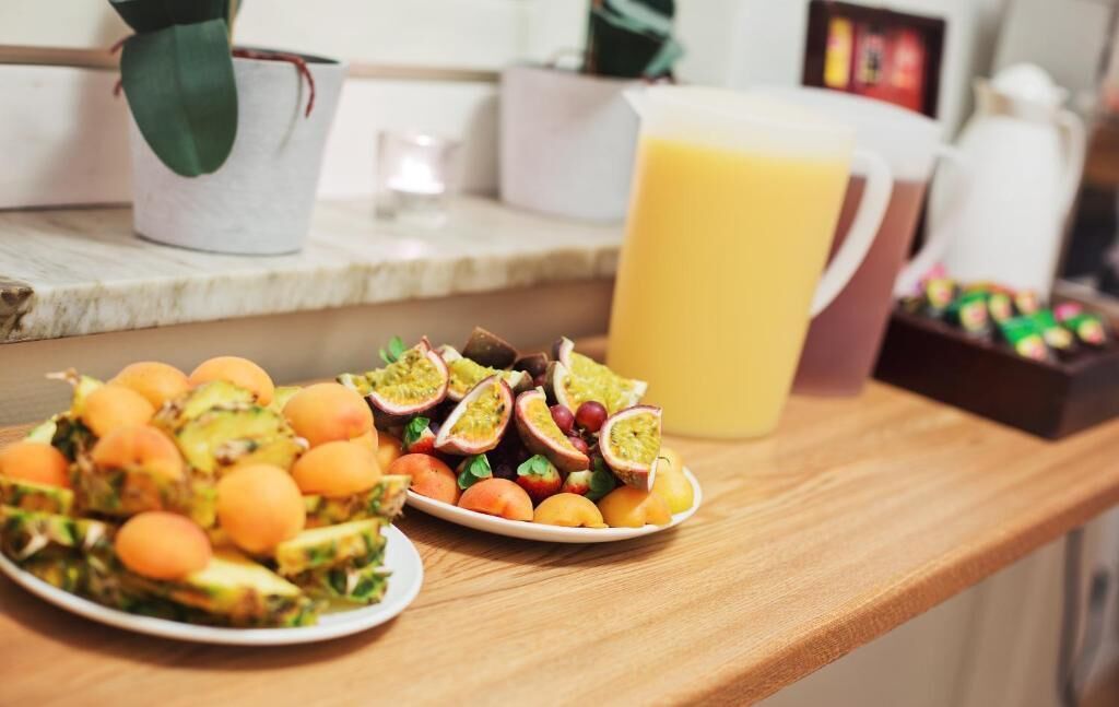 Un comptoir de cuisine avec une assiette de fruits coupés, une carafe de jus et une plante en pot.