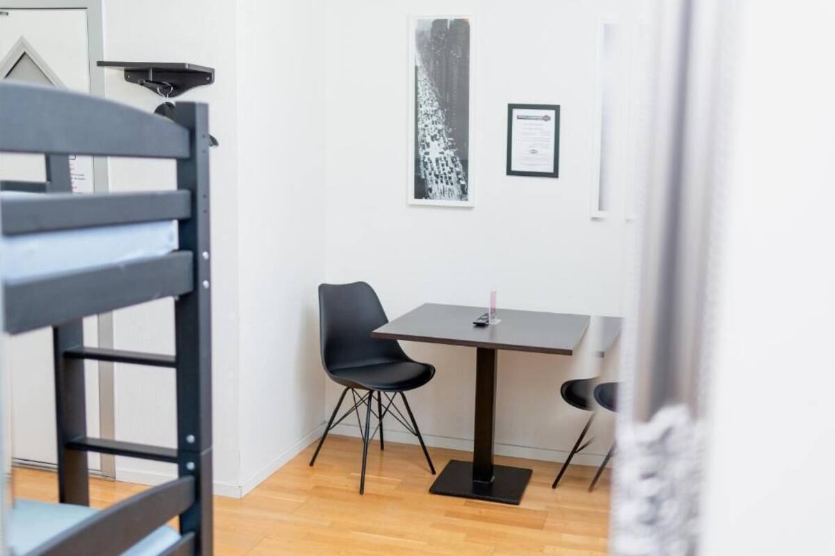 Une pièce avec un plancher en bois, un bureau à structure métallique noire, deux chaises noires et un tableau encadré au mur.
