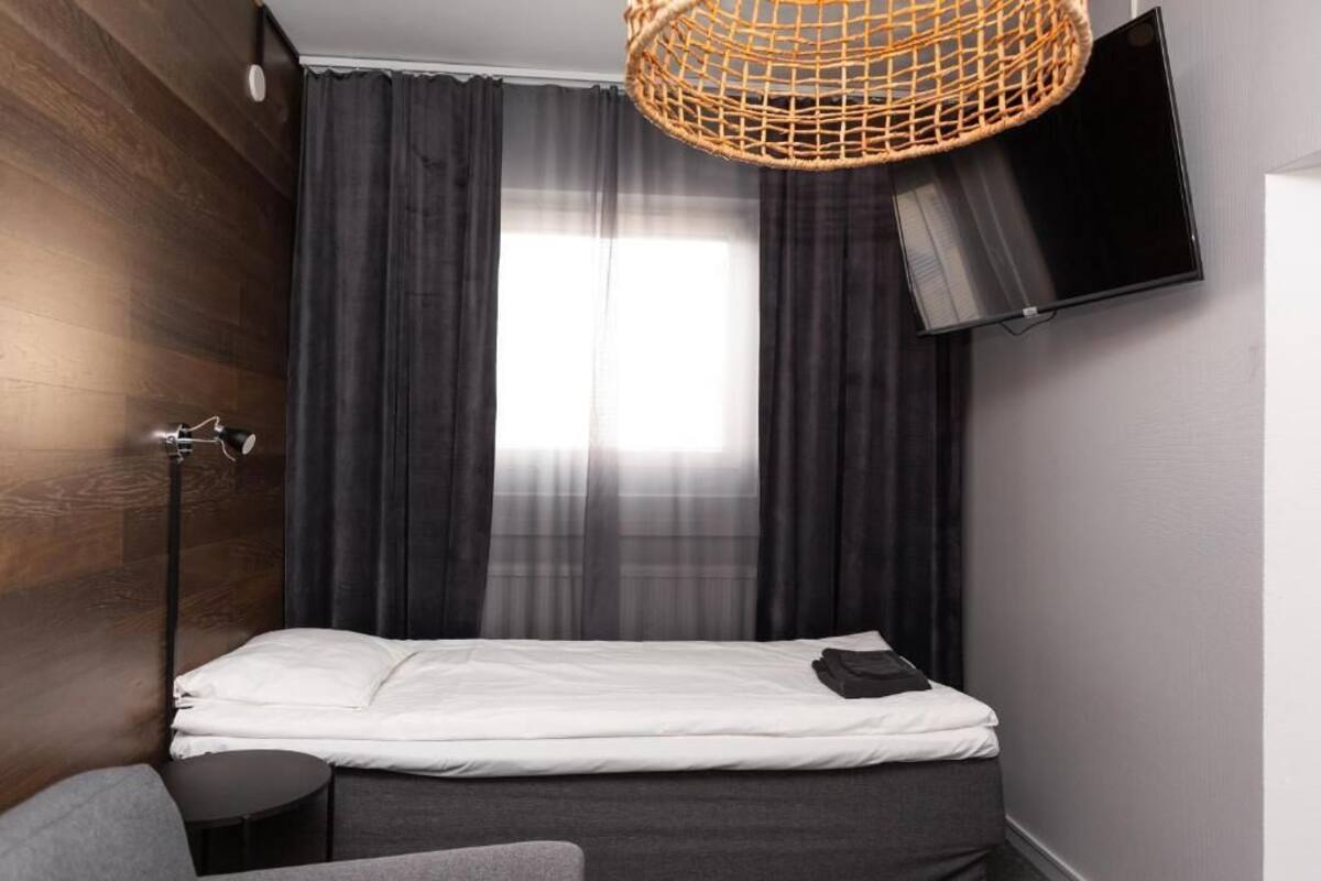 Une chambre à coucher avec un lit, une table ronde, une lampe sur pied, un téléviseur et une fenêtre avec des rideaux.