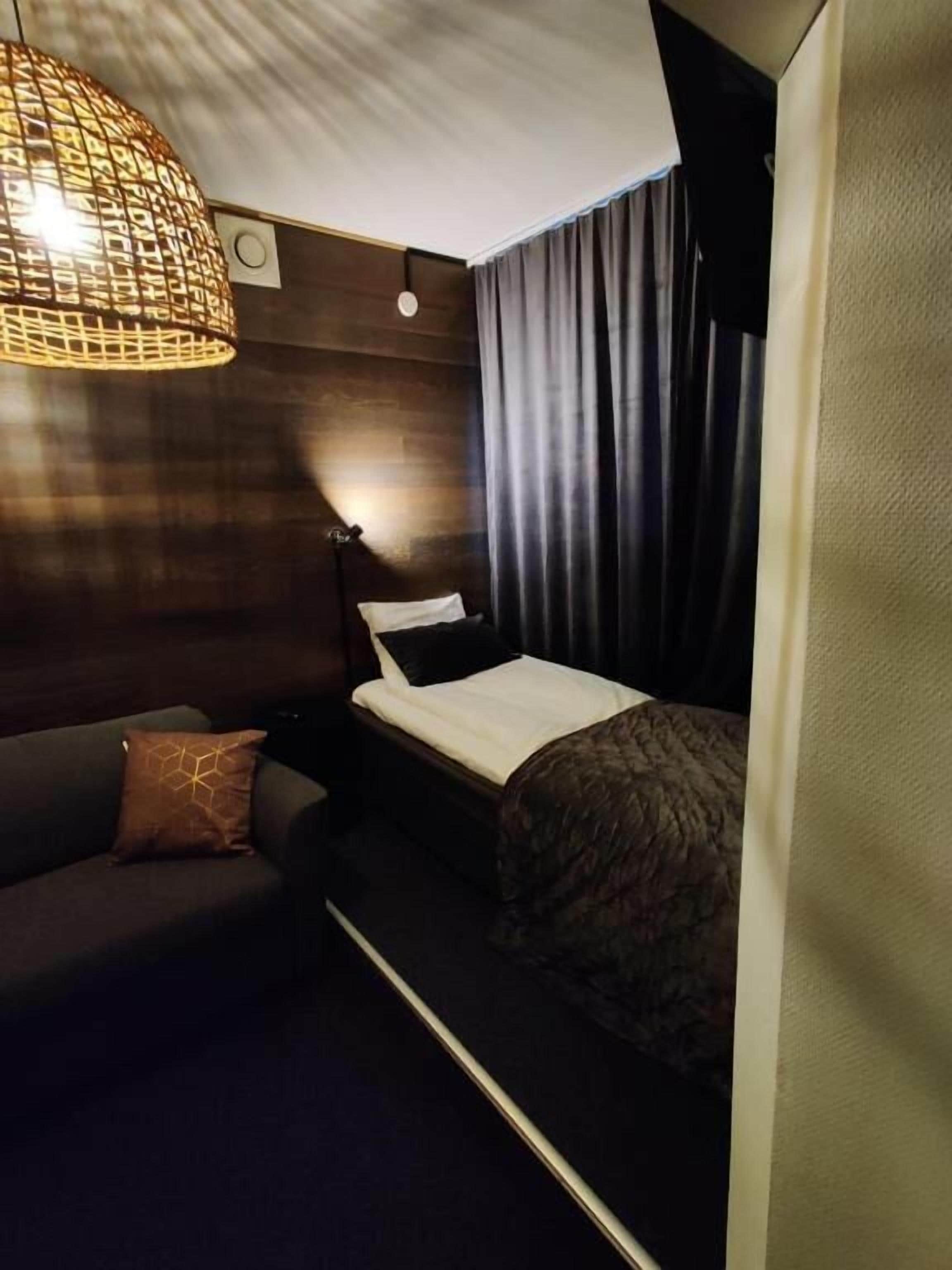 Een compacte hotelkamer met een bed, een slaapbank, een hanglamp en een gordijn.