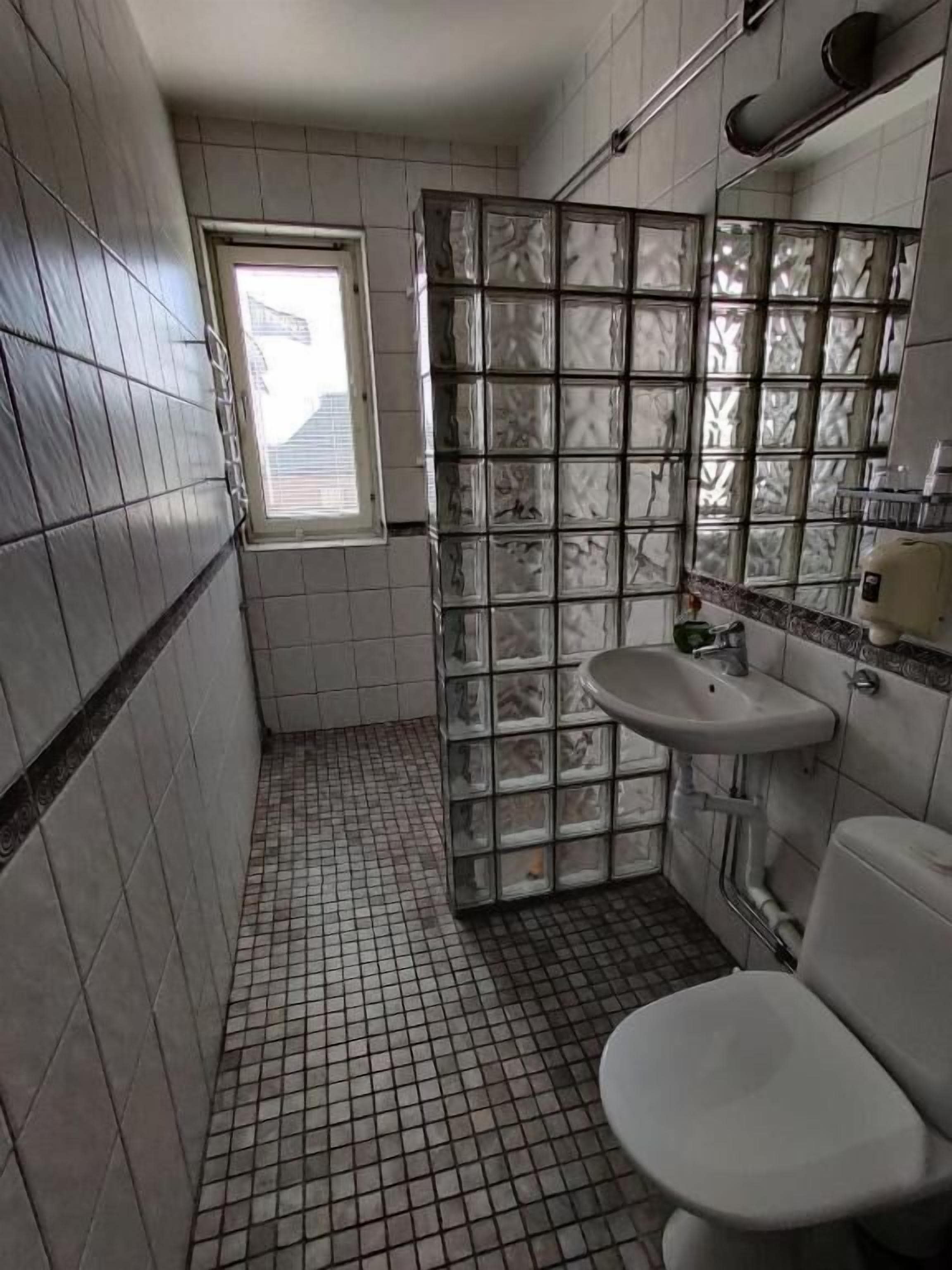 A small bathroom with a tiled floor, a toilet, a sink, and a window.