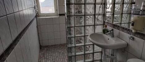 A small bathroom with a tiled floor, a toilet, a sink, and a window.