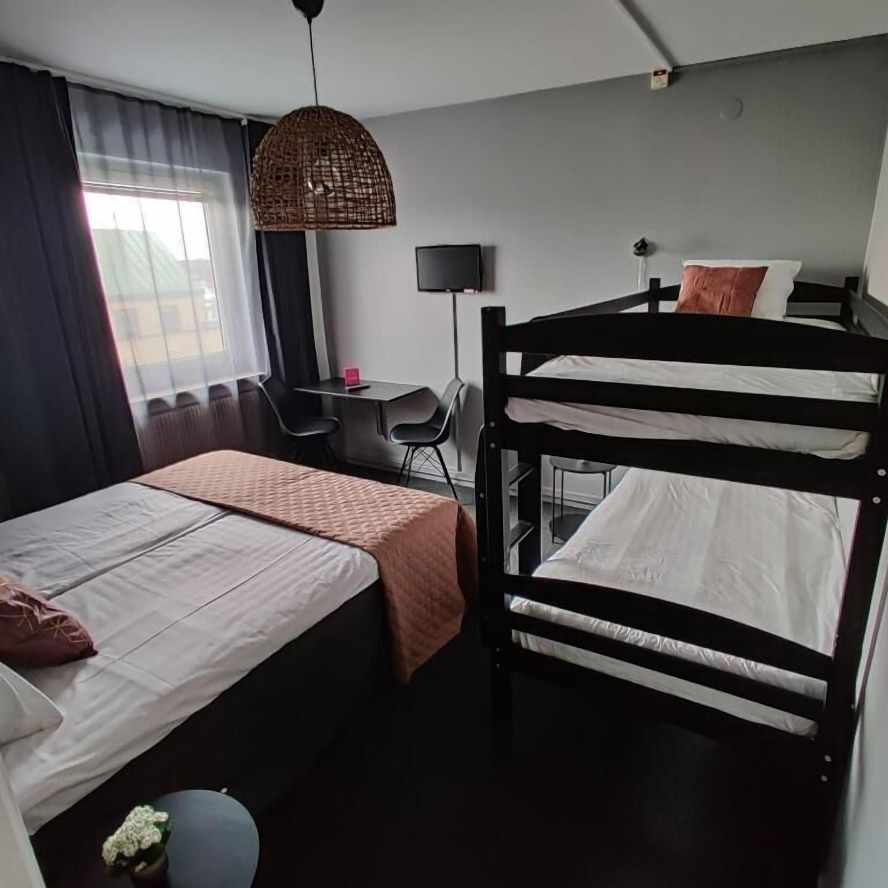 Ein Hotelzimmer mit einem Etagenbett, einem Schreibtisch mit Stuhl, einem Fernseher und einem Fenster mit Vorhängen.