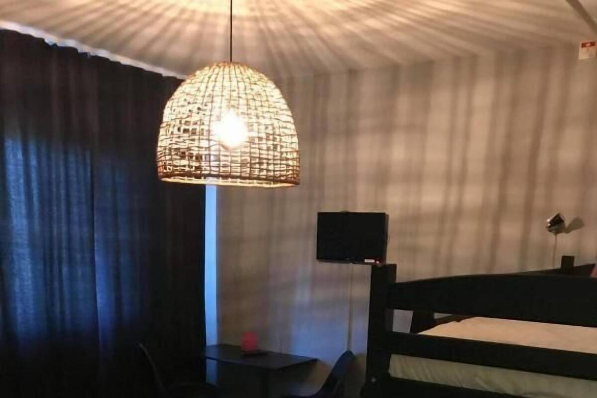 Une chambre d’hôtel avec des lits superposés, un bureau, une chaise, un téléviseur et un luminaire suspendu.
