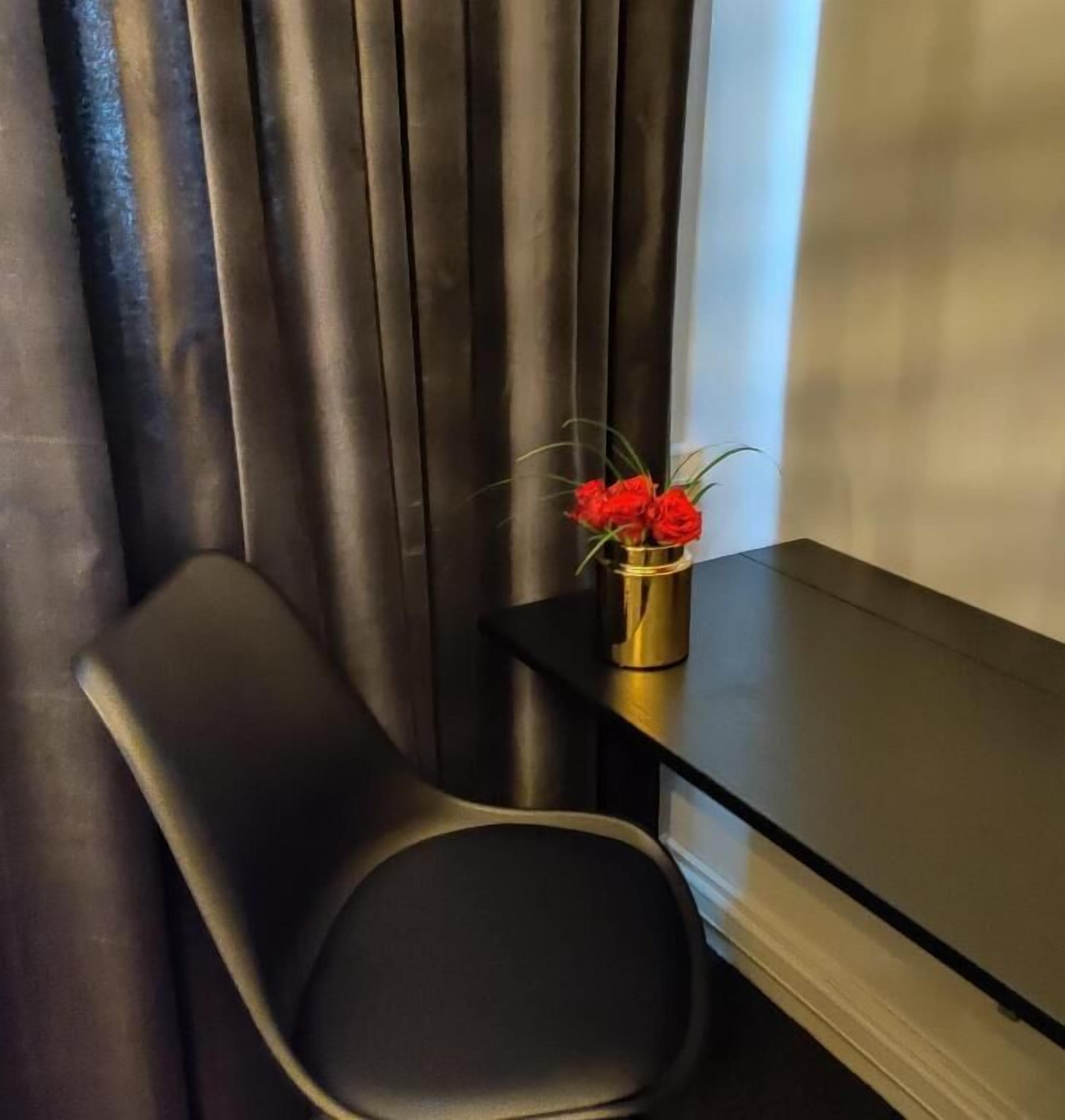 Une chambre moderne avec un fauteuil de couleur sombre, une petite table et un vase contenant des fleurs rouges.