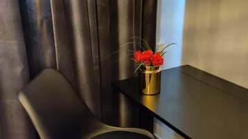 Une chambre moderne avec un fauteuil de couleur sombre, une petite table et un vase contenant des fleurs rouges.