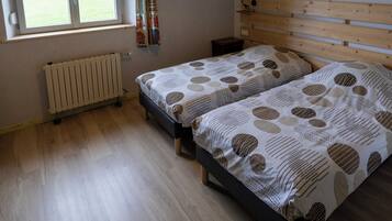 A bedroom with two beds, a wooden ceiling, a window with a view of a field, and a radiator.