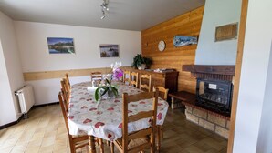 Un coin repas avec une table en bois, des chaises, une cheminée et deux tableaux encadrés au mur.